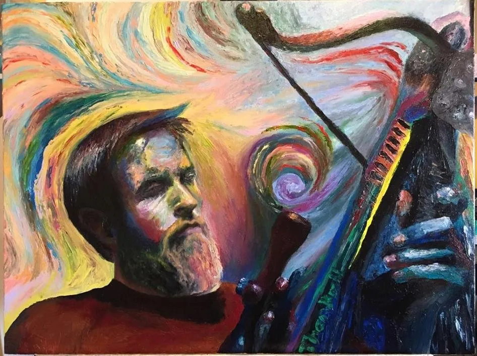 Bearded man in a red shirt in front of a harp, surrounded by swirling rainbow colors